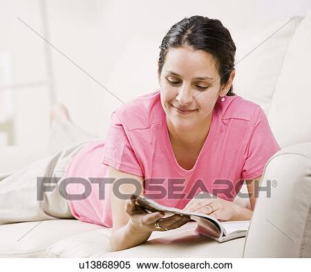 Stock Photography - Woman reading magazine on couch. Fotosearch