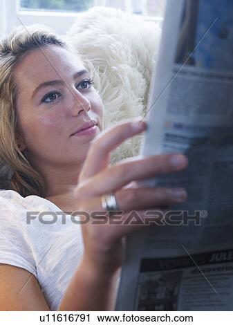 Stock Image - Woman reading newspaper on couch. Fotosearch