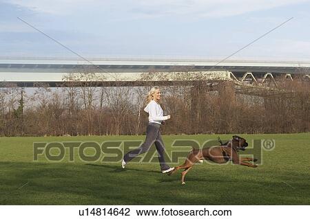 Stock Image - Woman running with dog in field. Fotosearch