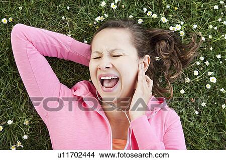 Picture - Woman singing to headphones in grass. Fotosearch