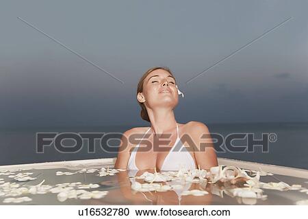 Stock Image - Woman sitting in pool with flowers. Fotosearch