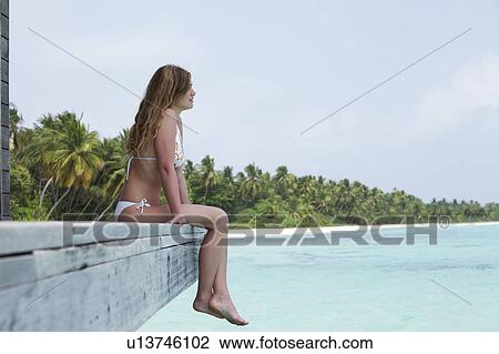 Stock Image - Woman sitting on deck overlooking beach. Fotosearch