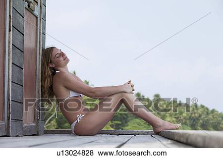 Stock Photo - Woman sitting on deck overlooking beach. Fotosearch