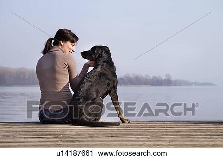 Stock Image - Woman sitting with dog on dock. Fotosearch