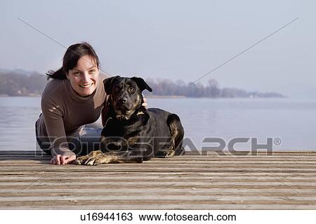 Stock Image - Woman sitting with dog on dock. Fotosearch