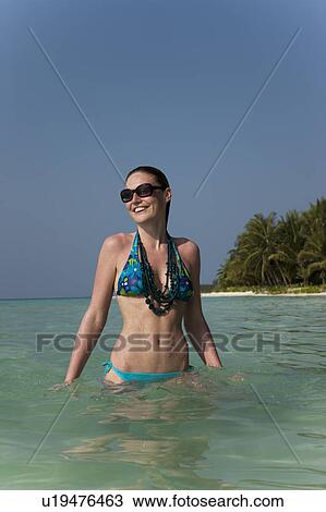 Stock Image - Woman standing in water on beach. Fotosearch
