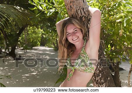 Stock Image - Woman standing under tree on beach. Fotosearch
