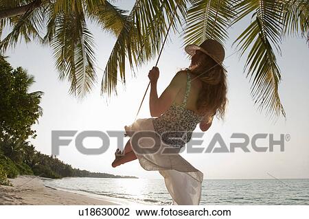 Stock Image - Woman swinging on tropical beach. Fotosearch