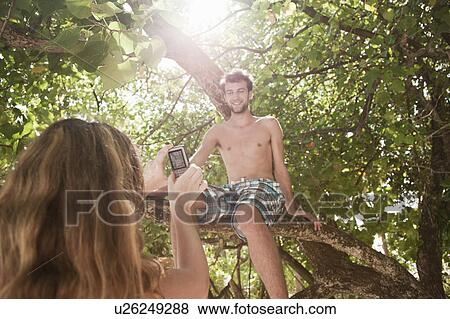 Stock Photo - Woman taking photo of boyfriend in tree. Fotosearch