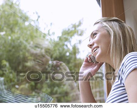 Woman talking on cell phone at window View Large Photo Image Stock Photograph - Woman talking on cell phone at window. Fotosearch