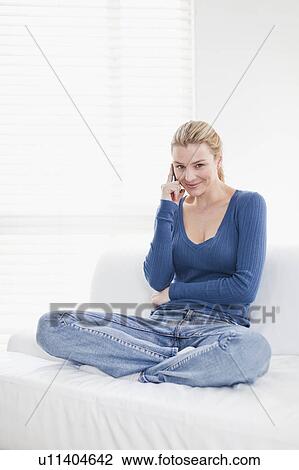 Stock Image - Woman talking on cell phone on couch. Fotosearch