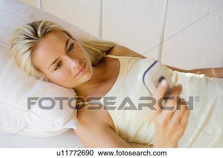 Stock Image - Woman using cell phone in bed. Fotosearch