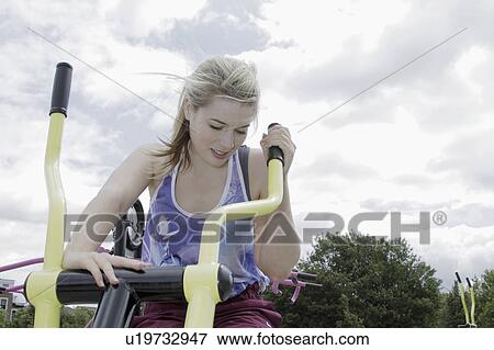 Stock Photo - Woman using exercise machine outdoors. Fotosearch