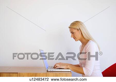 Stock Image - Woman using laptop at desk. Fotosearch