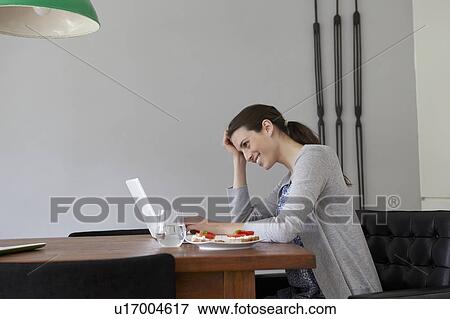 Stock Photo - Woman using laptop in dining room. Fotosearch