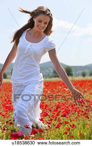 Stock Image - Woman walking in field of poppies. Fotosearch