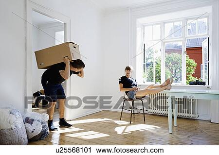 Stock Image - Woman watching boyfriend carry heavy box. Fotosearch