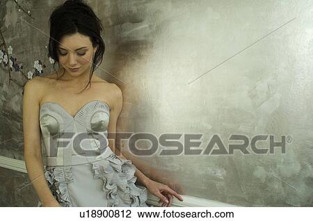 Stock Image - Woman wearing gown by ornate wallpaper. Fotosearch
