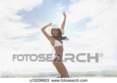Stock Image - Woman wearing sunhat and bikini on beach. Fotosearch