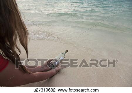 Stock Image - Woman with message in a bottle at beach. Fotosearch