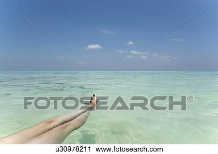 Stock Image - Woman’s legs floating in tropical sea. Fotosearch