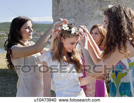 Stock Image - Women placing daisy crown on bride. Fotosearch