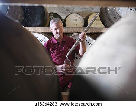 Stock Image - Worker checking whisky in distillery. Fotosearch