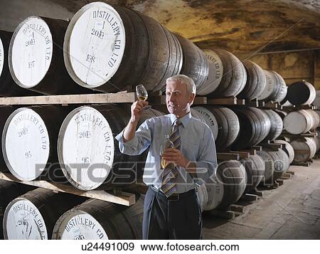 Stock Photo - Worker checking whisky in distillery. Fotosearch