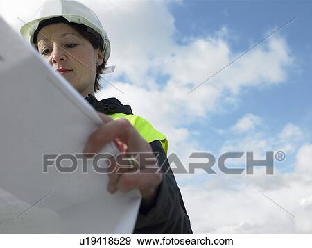 Stock Photo - Worker examining blueprints on site. Fotosearch