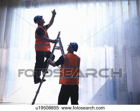 Stock Photography - Worker holding ladder for colleague. Fotosearch