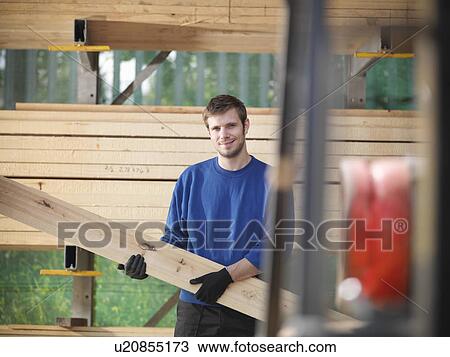 Stock Image - Worker holding planks of wood in joinery. Fotosearch