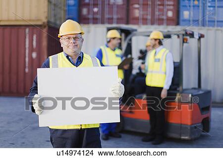Picture - Worker holding sheet in shipping yard. Fotosearch