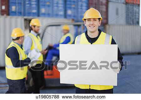 Stock Photo - Worker holding sheet in shipping yard. Fotosearch