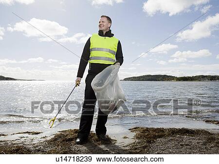 Stock Photo - Worker in safety vest cleaning beach. Fotosearch
