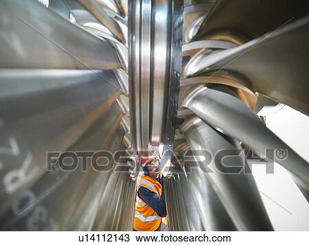 Stock Image - Worker inspects turbine in power station. Fotosearch