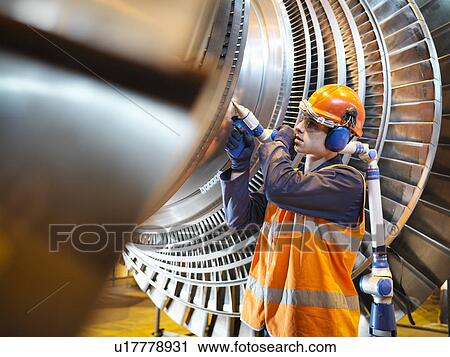 Stock Image - Worker inspects turbine in power station. Fotosearch