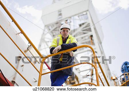 Stock Image - Worker leaning on railing of oil rig. Fotosearch