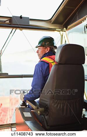Stock Image - Worker operating machinery on oil rig. Fotosearch