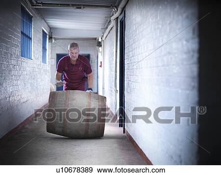 Stock Photo - Worker rolling whisky barrel. Fotosearch