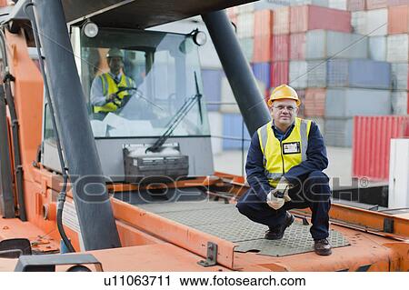 Stock Image - Worker standing on machinery on site. Fotosearch