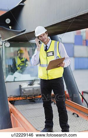 Stock Photograph - Worker standing on machinery on site. Fotosearch