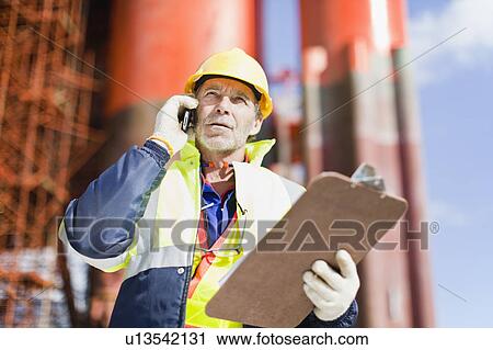 Worker talking on cell phone on oil rig View Large Photo Image Stock Image - Worker talking on cell phone on oil rig. Fotosearch