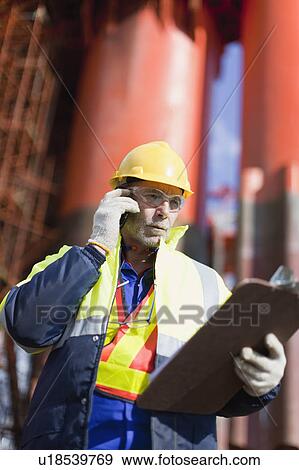 Worker talking on cell phone on oil rig View Large Photo Image Stock Photo - Worker talking on cell phone on oil rig. Fotosearch