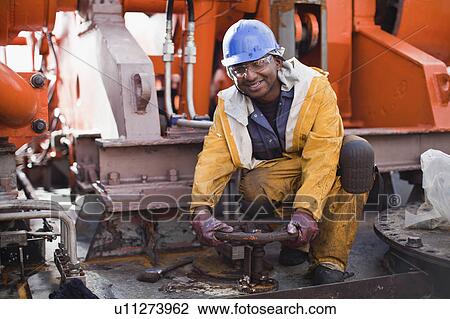 Stock Image - Worker turning wheel on oil rig. Fotosearch
