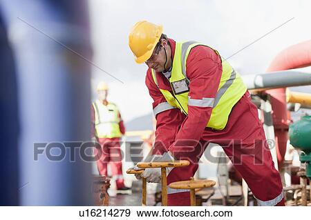Stock Photo - Worker turning wheel on oil rig. Fotosearch