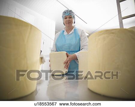 Stock Photo - Worker wrapping cheese in factory. Fotosearch