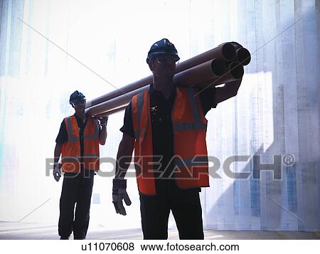 Stock Photo - Workers carrying pipes together. Fotosearch
