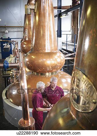Stock Image - Workers checking stills in distillery. Fotosearch