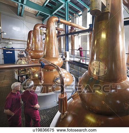 Stock Photography - Workers checking stills in distillery. Fotosearch