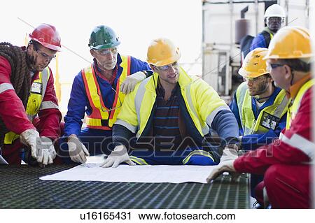 Stock Image - Workers examining blueprints on oil rig. Fotosearch
